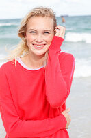 A young blonde woman by the sea wearing a red jumper