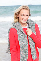 A young blonde woman wearing a red jumper with a grey jumper over her shoulders