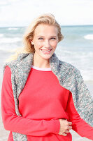 A young blonde woman wearing a red jumper with a grey jumper over her shoulders