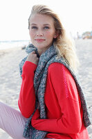 A young blonde woman wearing a red jumper with a grey jumper over her shoulders