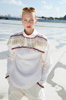 A young blonde woman wearing a white blouse with red beads