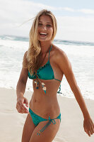 A blonde woman on a beach wearing a turquoise bikini