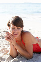 A mature brunette woman on a beach wearing a red bathing suit