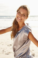 A mature blonde woman on a beach wearing a silver summer dress