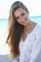 Junge blonde Frau in weißem Sommerkleid am Strand
