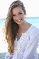 A young blonde woman on a beach wearing a white summer dress