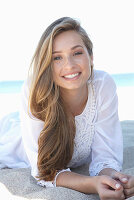 A young blonde woman on a beach wearing a white summer dress