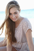 Junge blonde Frau in beigem Pünktchenkleid am Strand
