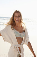 A mature blonde woman on a beach wearing lingerie and a cardigan