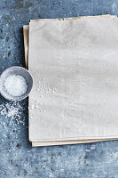 A dish of coarse sea salt next to multiple sheets of paper