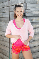 A brunette woman wearing a pink jumper, a top and shorts