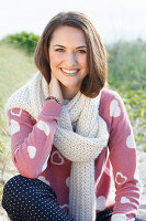 A brunette woman wearing a white scarf with a pink knitted jumper with hearts