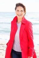 Brünette Frau in rotem Trenchcoat am Strand