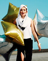 A young woman wearing a white hopped top and a black skirt with gold and silver balloons