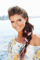 A young brunette woman with hair extensions by the sea wearing a colourful top