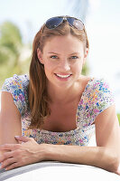 A young brunette woman outside wearing a colourful summer dress with sunglasses on her head