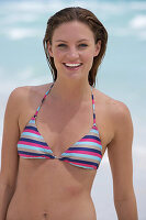A young brunette woman on a beach wearing a striped bikini