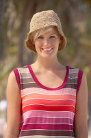 A mature blonde woman with short hair outside wearing a striped top and a hat