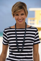 A young blonde woman with short hair on a beach wearing a black-and-white striped top