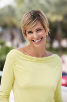 A young blonde woman with short hair outside wearing a yellow top