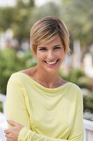 A young blonde woman with short hair outside wearing a yellow top