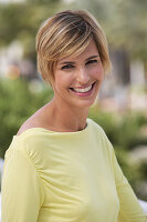 A young blonde woman with short hair outside wearing a yellow top