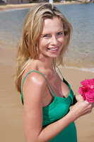 A young blonde woman on a beach wearing a green top and a pink bikini
