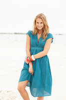 Junge blonde Frau im blauen Sommerkleid am Strand