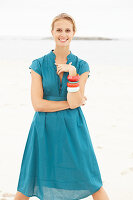 A young blonde woman on a beach wearing a blue summer dress