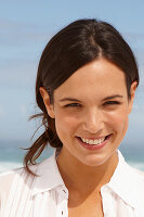 A young brunette woman on a beach wearing a white summer dress