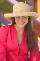 A young brunette woman wearing a dark pink blouse and a summer hat