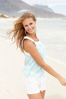 A young blonde woman on a beach wearing a light-blue top and white shorts
