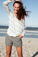 A brunette woman on a sandy beach wearing a striped top and shorts