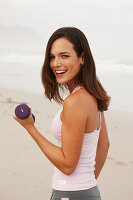 A young brunette woman on a beach wearing a sports outfit with a dumbbell