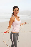 Junge brünette Frau im Sportoutfit und mit Sprungseil am Strand