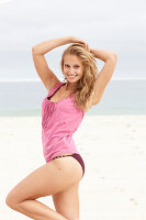 A young blonde woman on a beach wearing a pink top and a bikini