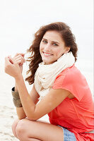 A brunette woman on a beach wearing a scarf and a salmon-coloured top