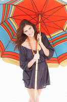 Brünette Frau im lila Strandkleid mit buntem Sonnenschirm