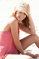 A young blonde woman on a beach wearing a pink top and a beige hat