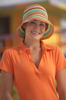 A young brunette woman wearing an orange polo shirt with a colourful summer hat