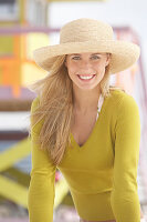 Junge blonde Frau mit olivfarbenem Shirt und beigem Sonnenhut am Strand