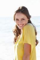 Junge brünette Frau im gelben Sommerkleid am Strand