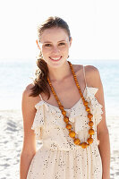 A young brunette woman on a beach wearing a light summer dress and a necklace
