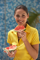 A young brunette woman wearing a yellow polo shirt and holding a slice of watermelon