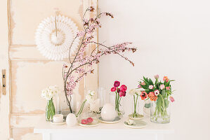 Ranunkeln, Tulpen und Blütenzweig in Glasvasen auf österlichem Tisch