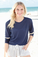 A young blonde woman on a beach wearing a long-sleeved blue shirt and shorts