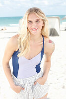 Junge blonde Frau mit Tattoo im Badeanzug und Shorts am Strand