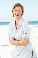 A mature woman with short blonde hair on a beach wearing a light-blue striped short