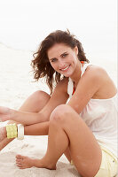 A brunette woman on a beach wearing a white top and shorts