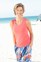A mature woman on a beach wearing a salmon-coloured top and colourful trousers
